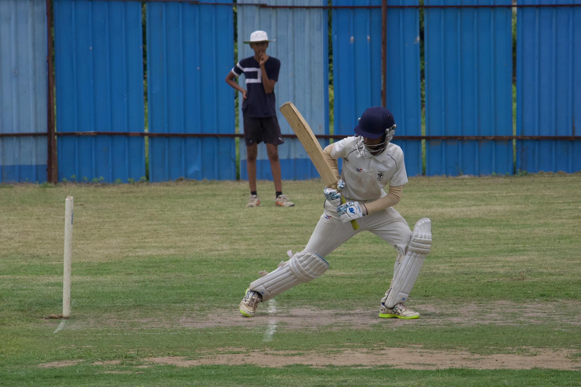 Cricket player batting on a grass field in Gahunje, India, showcasing dynamic sports action. - 11 Dead in Stampede Outside India Cricket Stadium