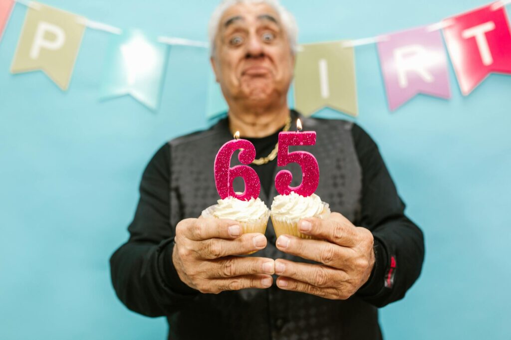 Senior man holding cupcakes with 65 candle during his birthday celebration.