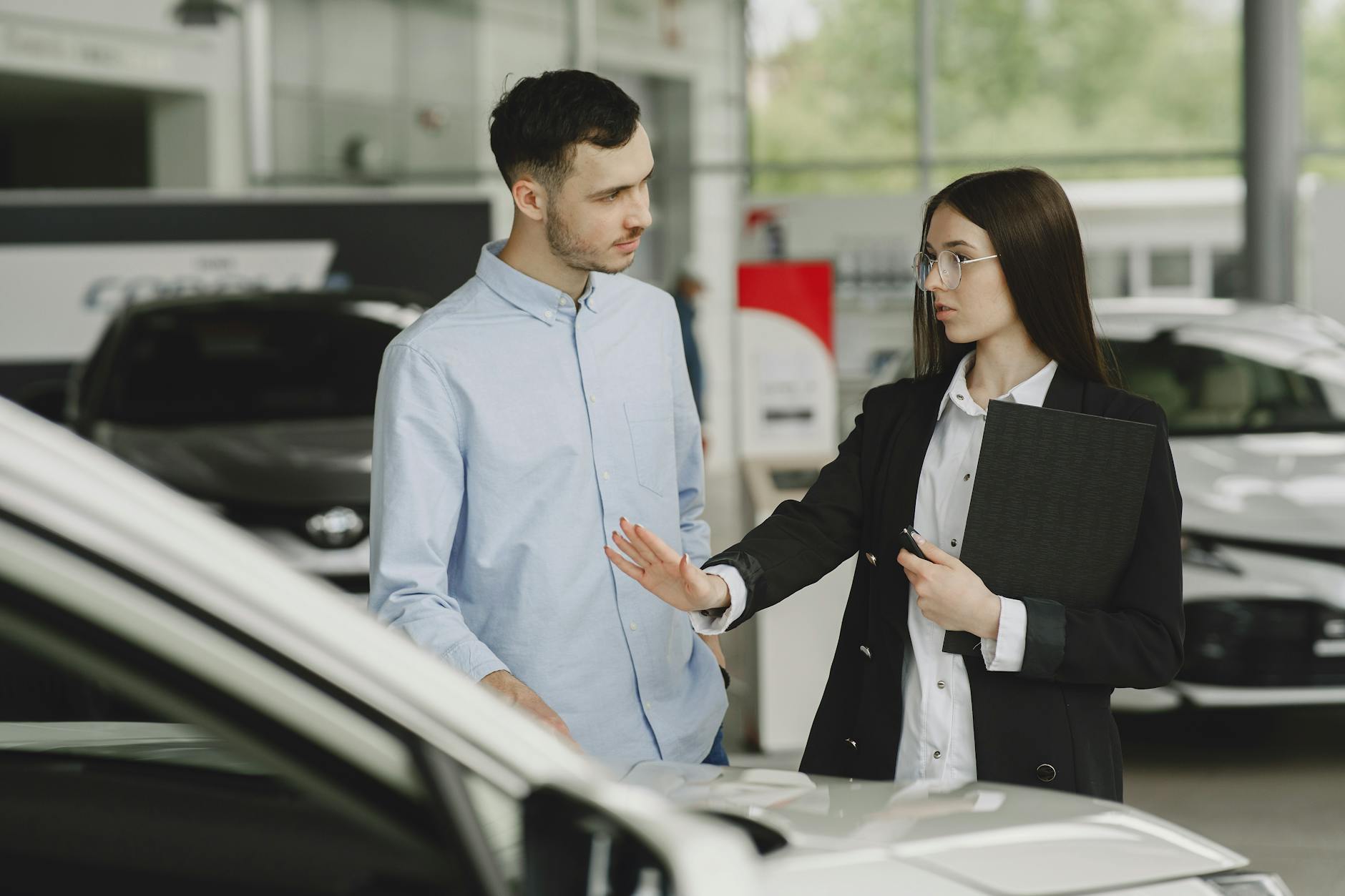 Top 4 Auto Stocks to Buy After May Sales Data: Maruti to Escorts 3 A salesperson and customer discussing car features in a dealership setting. - Top 4 Auto Stocks to Buy After May Sales Data: Maruti to Escorts